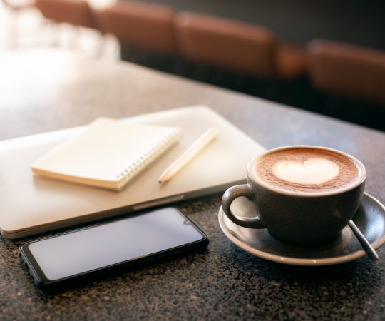 Work from home, desk office with blank notepad and pen on laptop with mobile phone and coffee drink with heart shape of latte